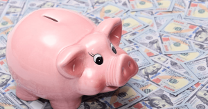 Pink piggy bank sitting on scattered US $100 bills, symbolizing savings and personal finance in action.